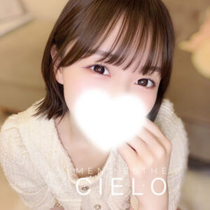 横浜センター南メンズエステCIELO | センター南シエロ Close-up portrait of a young woman with short brown hair in a light knit sweater, mouth softly obscured by a bright white glow, with the brand name 'CIELO' overlaid.